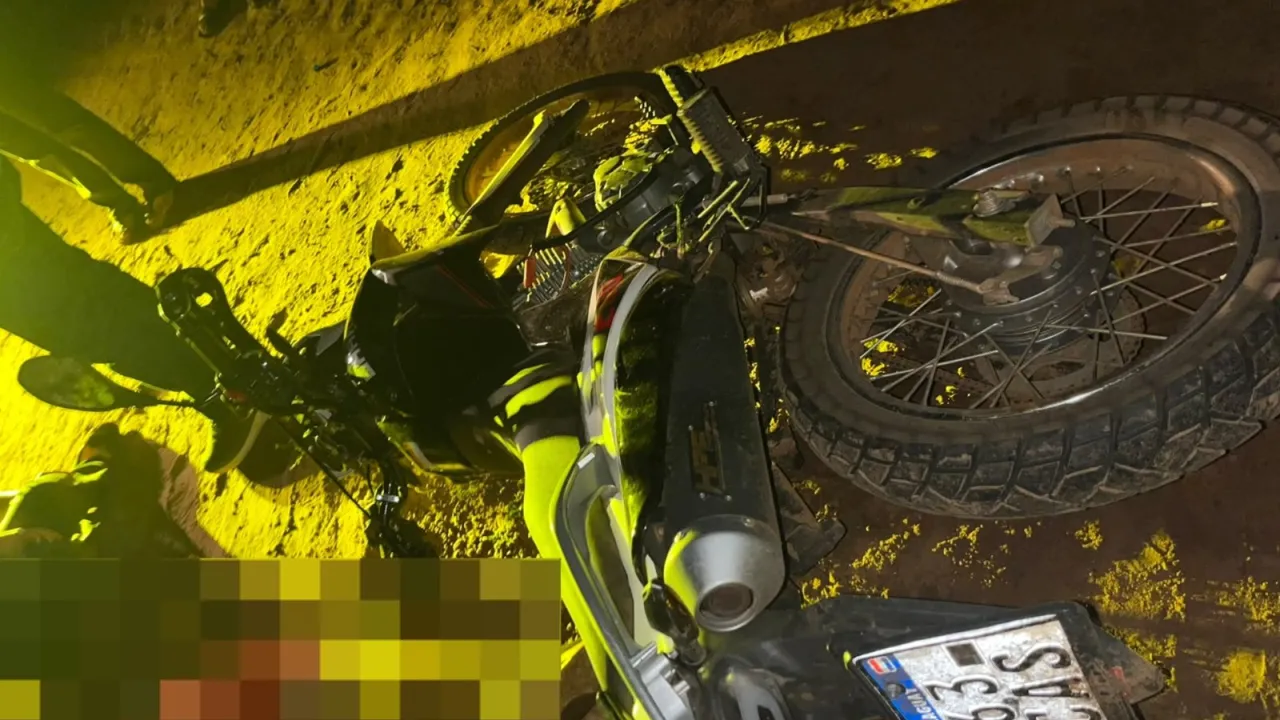 Motocicleta caída sobre un camino de tierra durante un procedimiento policial nocturno con iluminación artificial.
