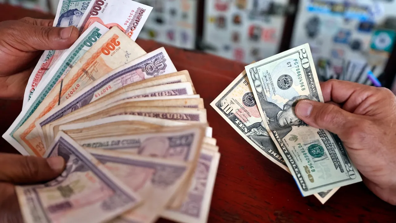 Persona sostiene un fajo de billetes de pesos cubanos en una mano y billetes de dólares en la otra.