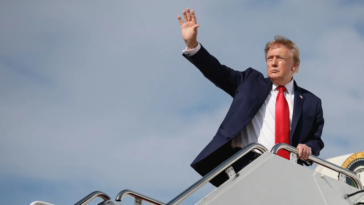 Donald Trump con traje oscuro y corbata roja saluda con la mano en alto desde la escalerilla de un avión oficial.