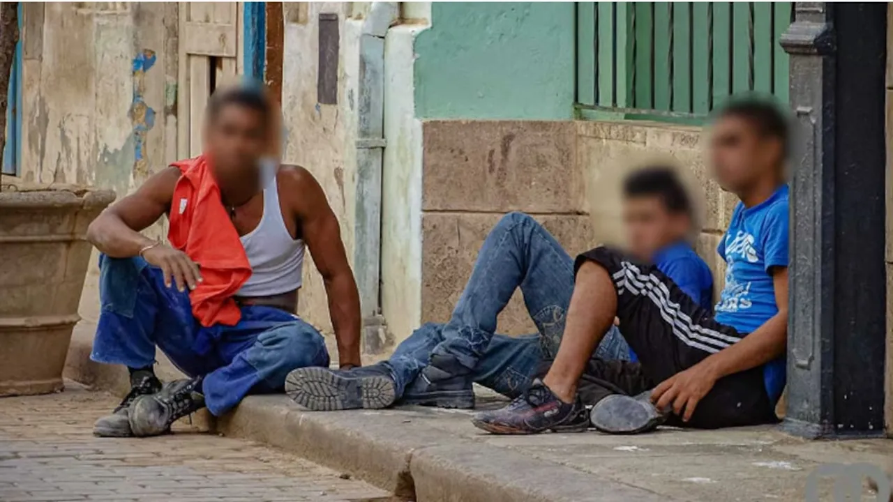 Tres jóvenes sentados en el cordón de una vereda de una calle urbana con los rostros difuminados.