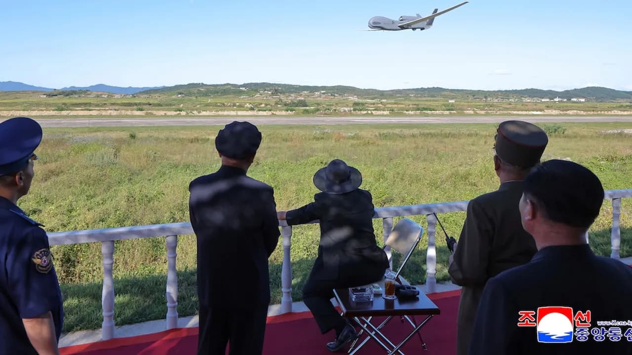Autoridades observan el vuelo de una aeronave militar no tripulada desde una pista abierta hacia un campo despejado.