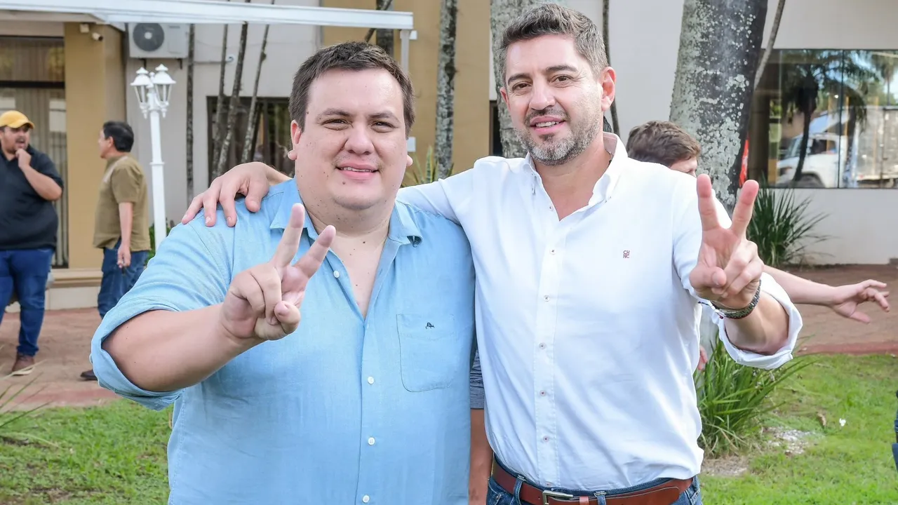 César Sosa y Pedro Alliana posan sonrientes en un jardín mientras realizan el gesto de la victoria con los dedos.