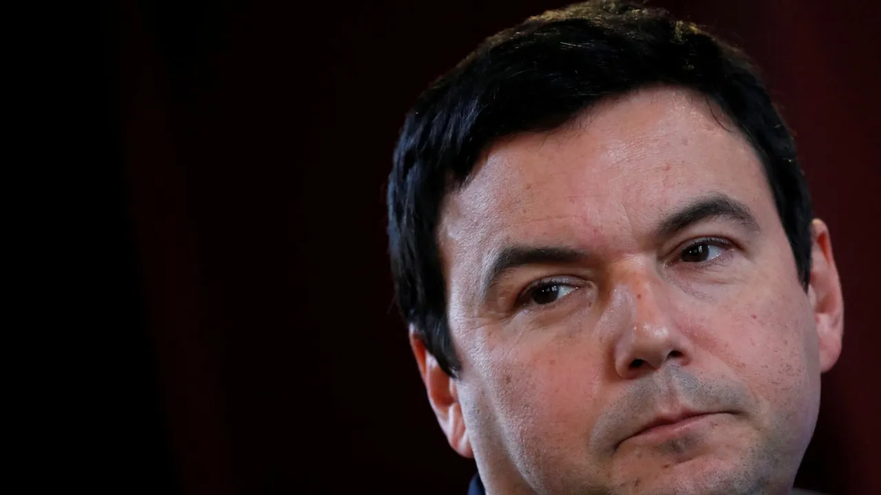 Primer plano del rostro del economista con gesto reflexivo y mirada hacia un costado sobre fondo oscuro.