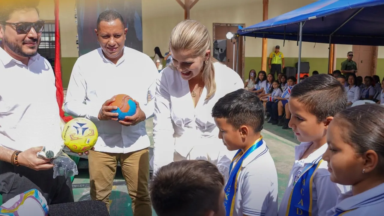 Autoridades entregan balones deportivos a estudiantes uniformados en el patio de una escuela al aire libre.