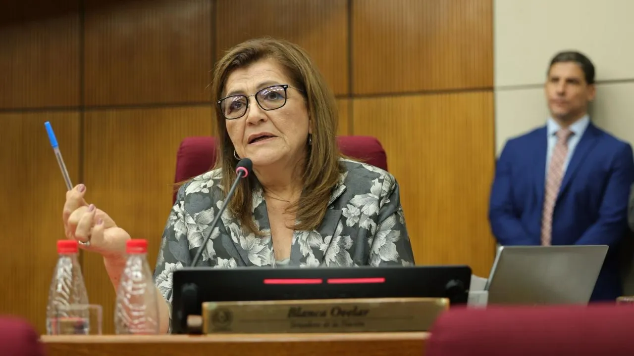 Blanca Ovelar sentada en su banca del Senado con micrófono al frente, sosteniendo un bolígrafo en la mano.