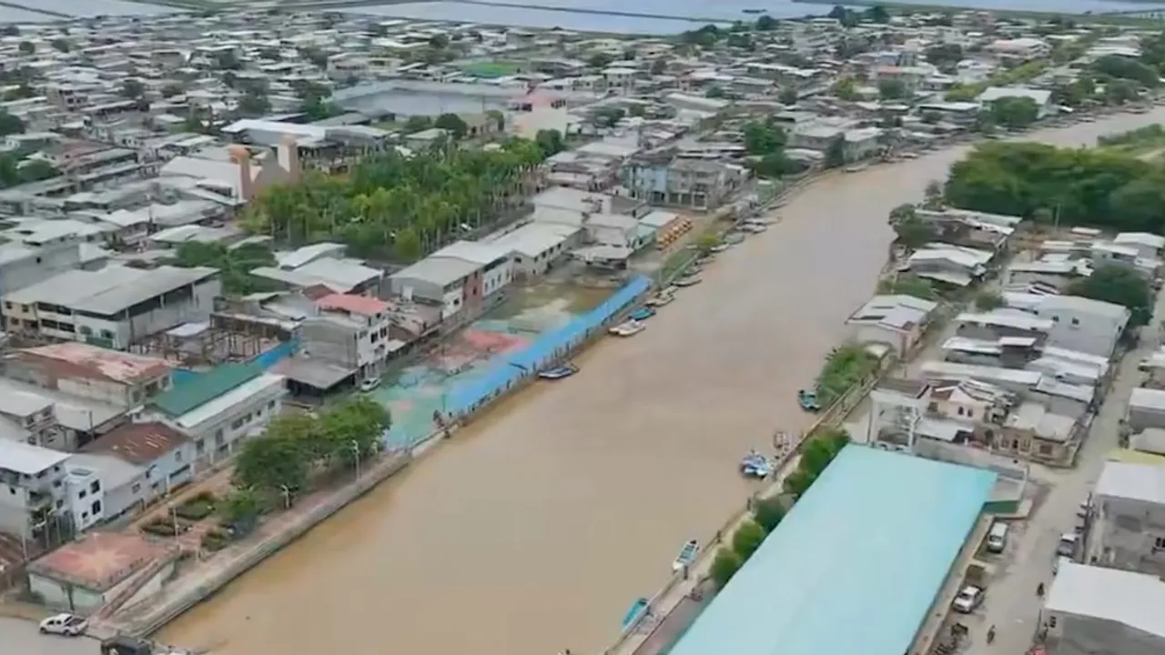 Vista aérea de un río crecido y turbio que cruza una zona urbana con viviendas y embarcaciones pequeñas.