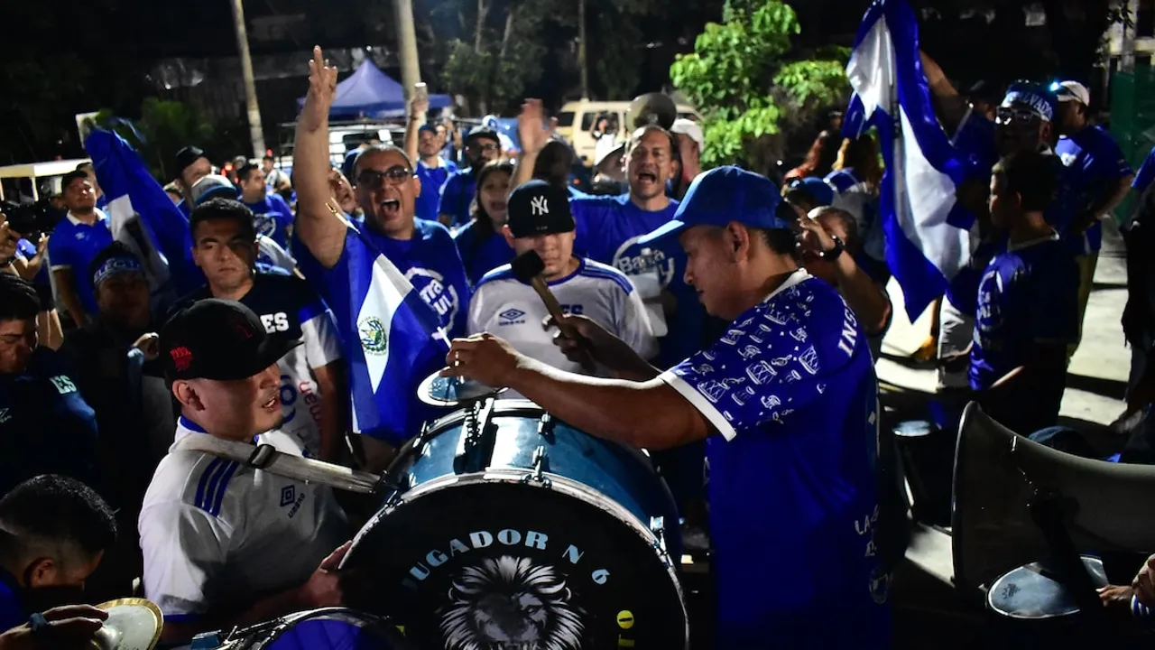Aficionados vestidos de azul tocan bombos e instrumentos metálicos mientras ondean banderas patrióticas en la calle.