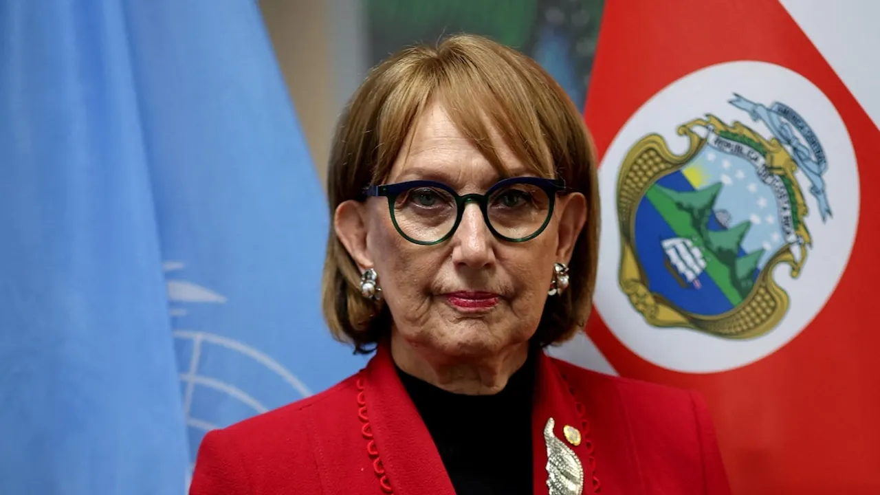 Rebeca Grynspan con anteojos oscuros y saco rojo posa frente a las banderas de la ONU y de Costa Rica.