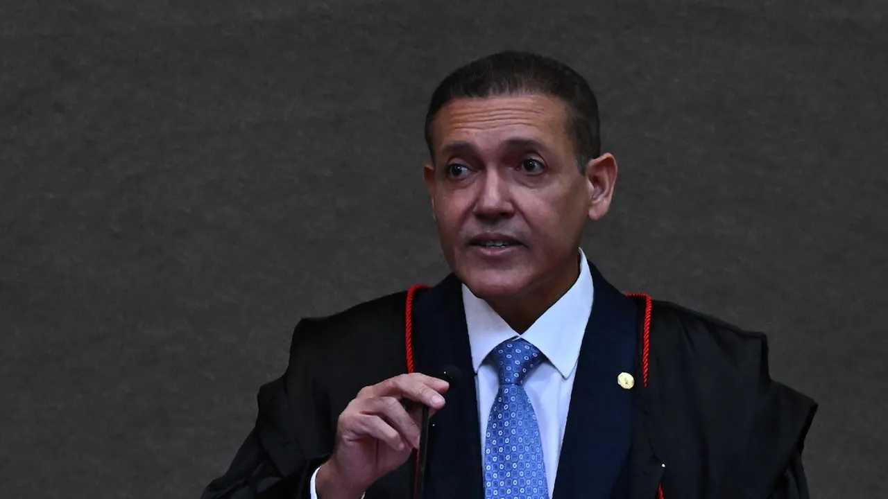 Hombre con toga jurídica negra y corbata azul habla frente a un micrófono en un recinto institucional.