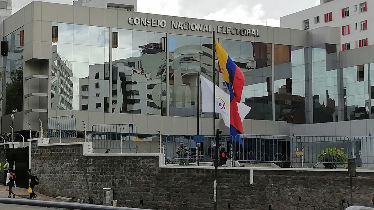 Edificio institucional con fachada acristalada, letrero del Consejo Nacional Electoral y banderas en la entrada.