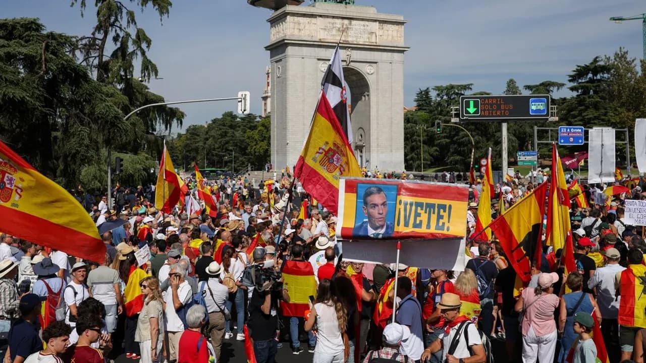 Manifestantes con banderas españolas y carteles contra el presidente del Gobierno frente a un monumento en Madrid.