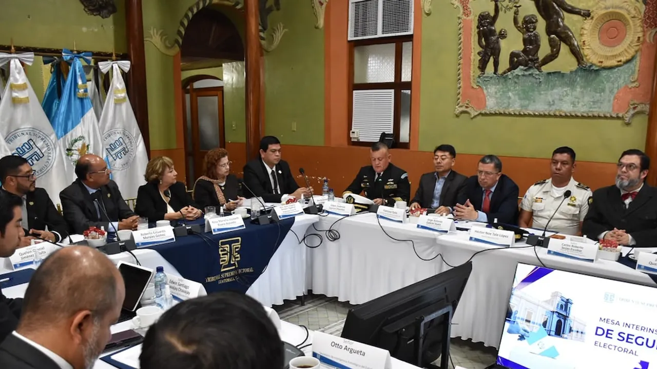 Autoridades electorales y de seguridad en una mesa de trabajo institucional con banderas y micrófonos.