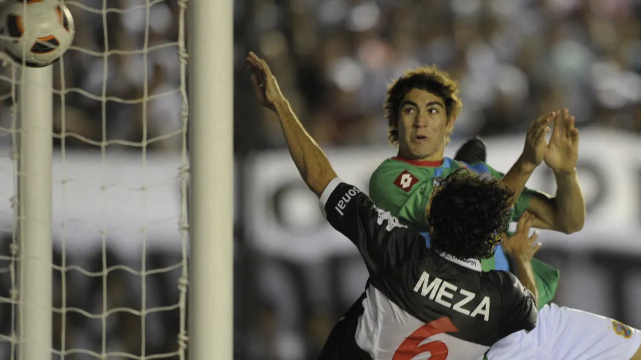 Disputa aérea dentro del área entre un delantero de Arsenal y un zaguero de Olimpia junto al arco.