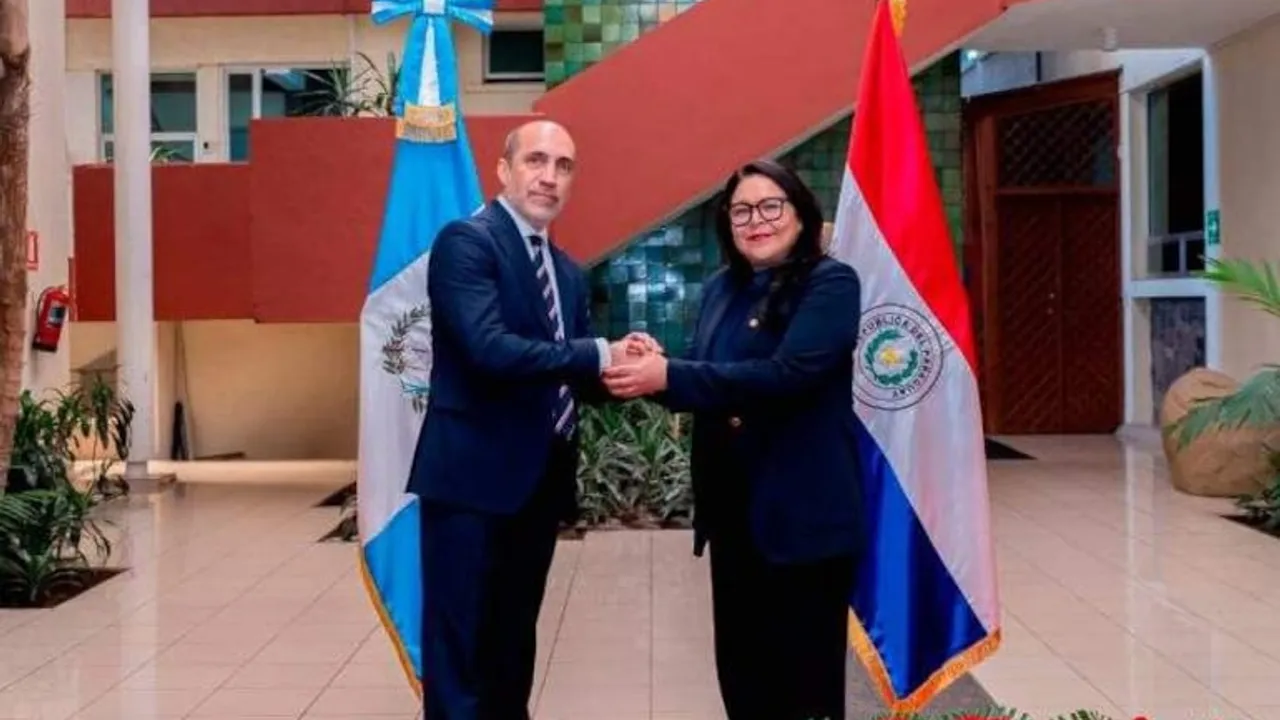 Víctor Verdún y Mónica Bolaños se estrechan la mano frente a las banderas oficiales de Paraguay y Guatemala.