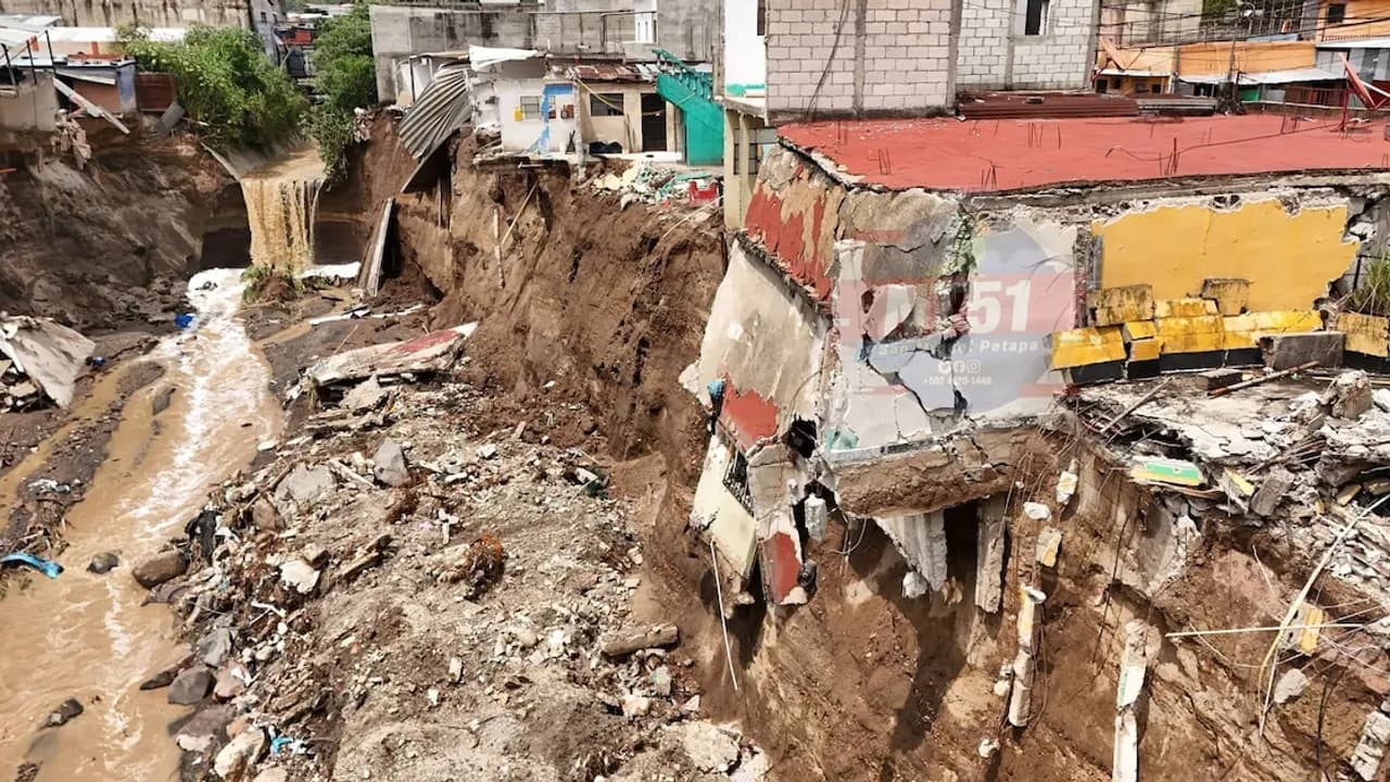 Casas al borde de un profundo barranco erosionado junto a un río turbio con escombros de viviendas derrumbadas.