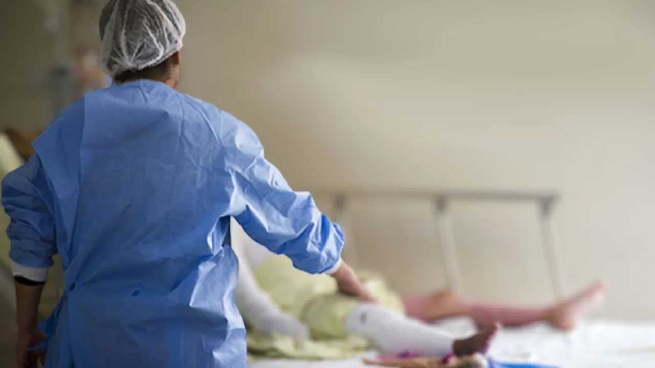 Personal médico con bata quirúrgica azul camina junto a una camilla hospitalaria donde reposa un paciente.