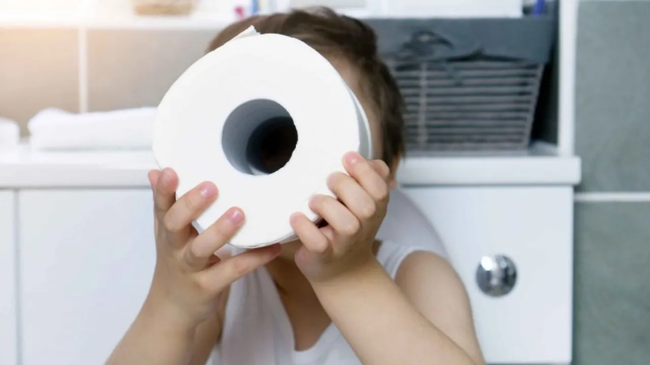 Un niño sostiene un rollo de papel higiénico blanco frente a su rostro en el interior de un baño.