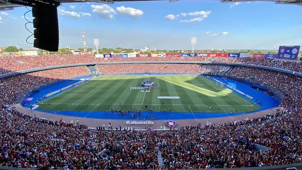 Tribunas repletas de hinchas en el estadio La Nueva Olla durante un partido de fútbol diurno.