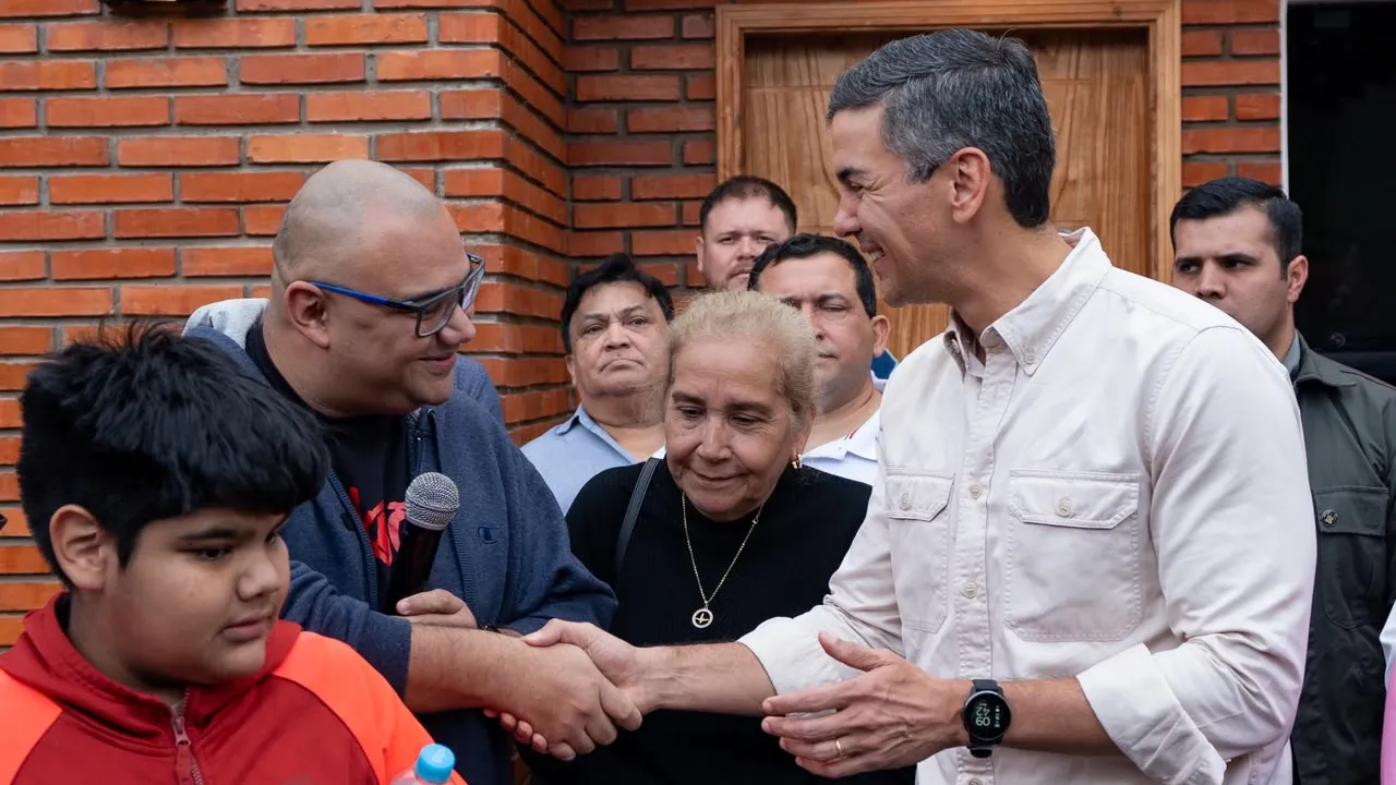 Santiago Peña saluda cordialmente a un poblador durante un acto oficial frente a una vivienda de ladrillos.