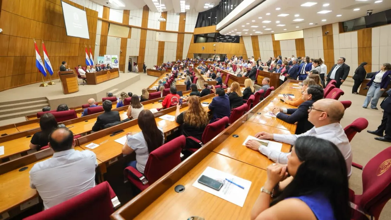 Personas sentadas en las bancas de una sala legislativa amplia durante el congreso sobre migración paraguaya