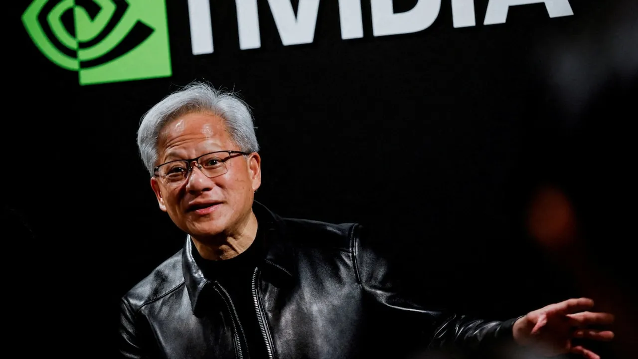Jensen Huang con chaqueta de cuero negra y anteojos gesticula frente al logotipo de Nvidia en un evento público.