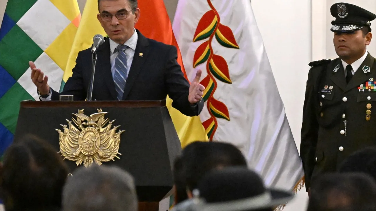 Rodrigo Paz discursa tras un podio oficial con escudo junto a un uniformado y banderas nacionales.