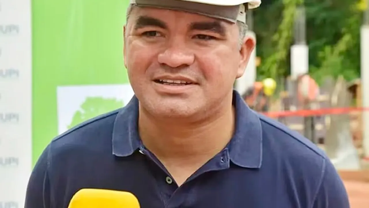 Hombre con casco blanco de obra y chomba azul oscura habla frente a un micrófono amarillo.