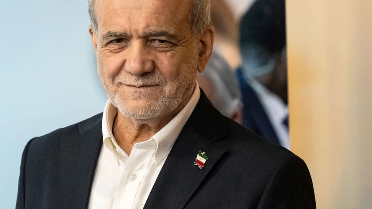 Masoud Pezeshkian viste traje formal oscuro, camisa blanca abierta en el cuello y un pin metálico con la bandera iraní.