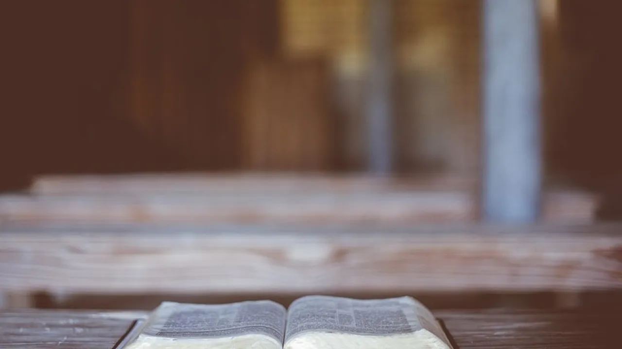 Biblia abierta sobre un banco rústico de madera en el interior iluminado de una capilla silenciosa.