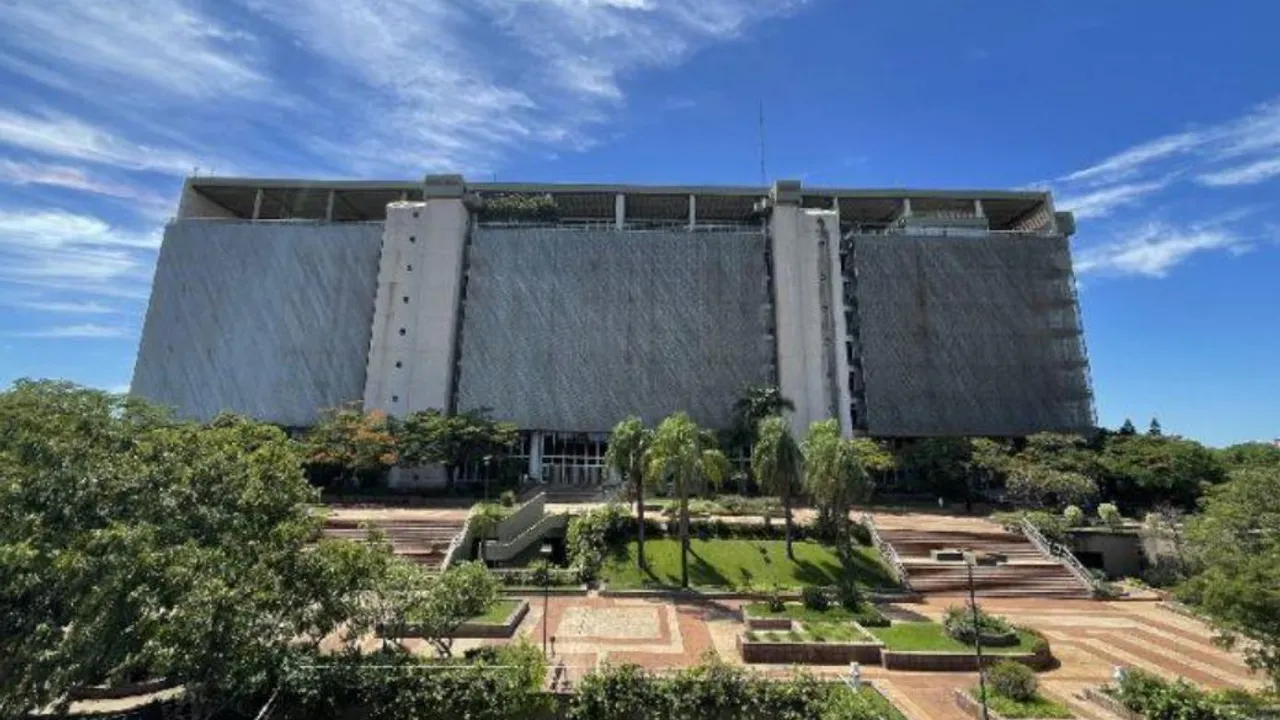 Fachada principal y jardines del edificio del Banco Central del Paraguay bajo un cielo despejado con nubes dispersas.