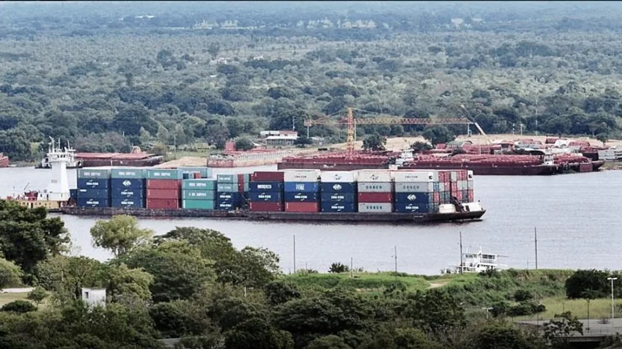 Barcaza cargada con contenedores de mercancías navegando por aguas fluviales cerca de la costa.