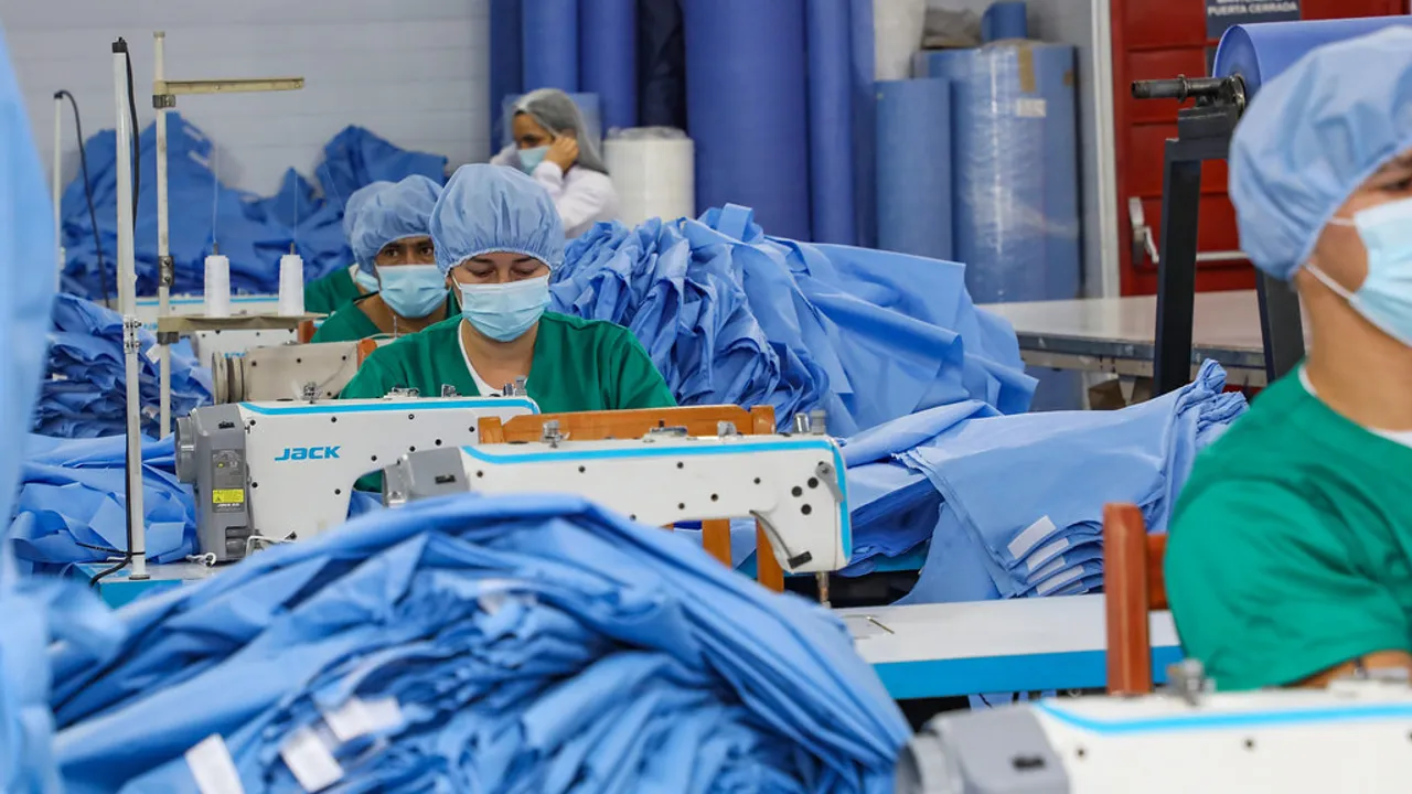 Trabajadoras operan máquinas de coser industriales confeccionando prendas en un taller textil.