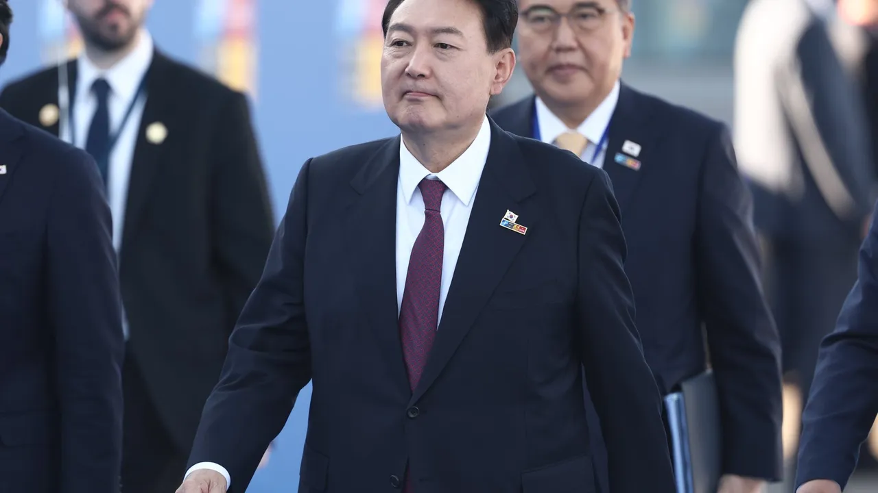 Yoon Suk Yeol camina en traje oscuro y corbata roja con pin de bandera en la solapa escoltado por comitiva.