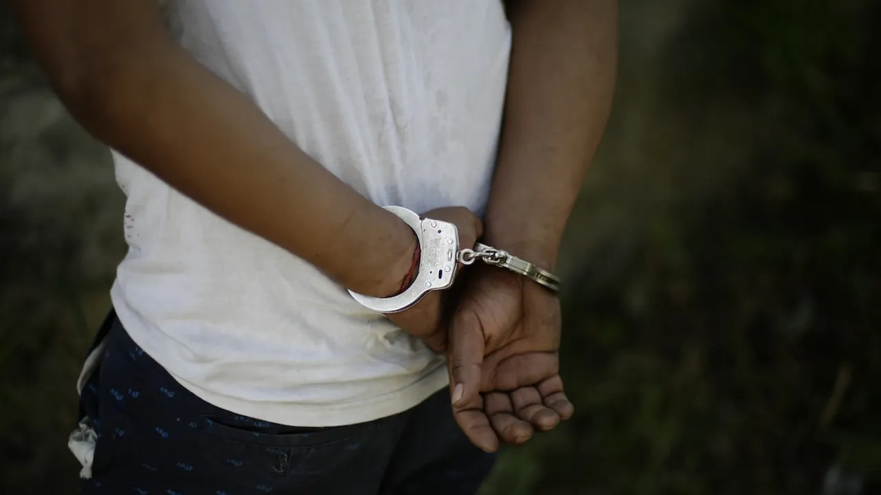 Primer plano de una persona de espaldas con las manos esposadas detrás de la cintura vistiendo una remera blanca