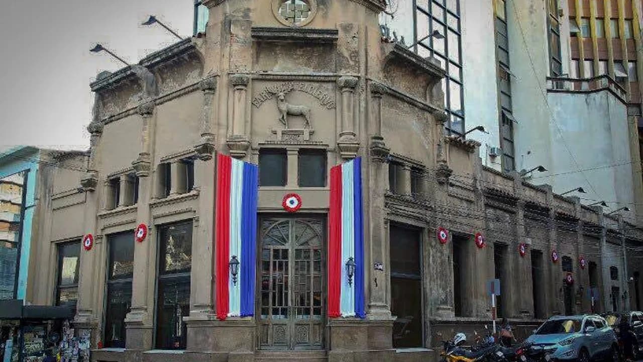 Fachada histórica de un edificio antiguo con banderas paraguayas y decoraciones patrias en su entrada