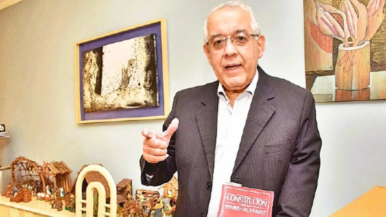 Luis Lezcano Claude con traje oscuro y anteojos sostiene un ejemplar de la Constitución Nacional