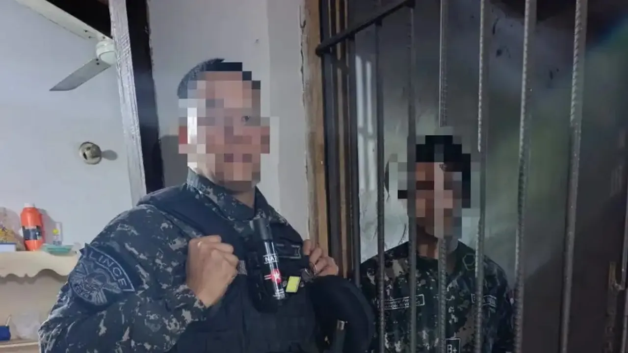 Dos hombres con uniformes tácticos y rostros cubiertos permanecen junto a las rejas de una dependencia.