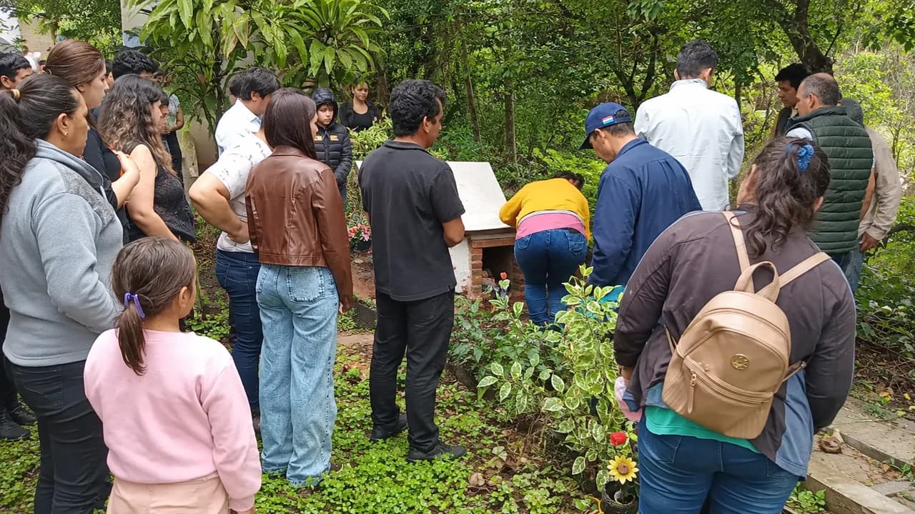 Grupo de personas reunidas en un entorno arbolado durante el sepelio en el cementerio