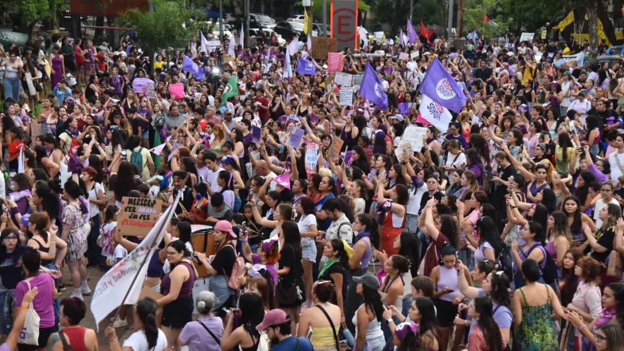 Multitud de mujeres congregadas en una manifestación portando banderas moradas y carteles en un espacio público.