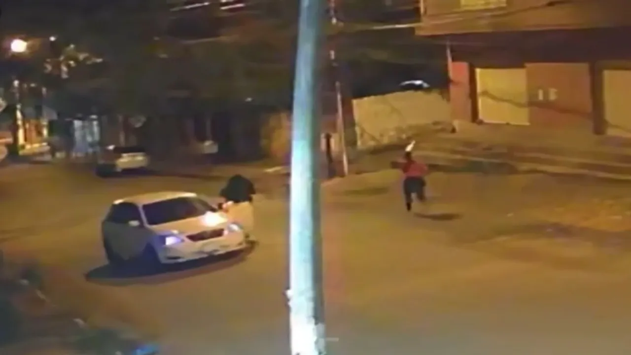 Captura nocturna de cámara de seguridad que muestra a una persona corriendo en la calle junto a un vehículo blanco.