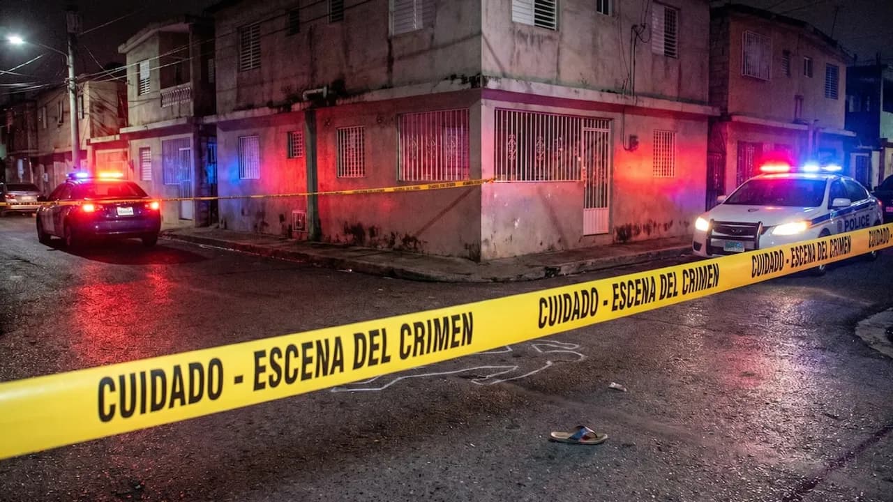 Cinta policial amarilla de escena del crimen en una calle nocturna custodiada por patrullas con balizas encendidas.
