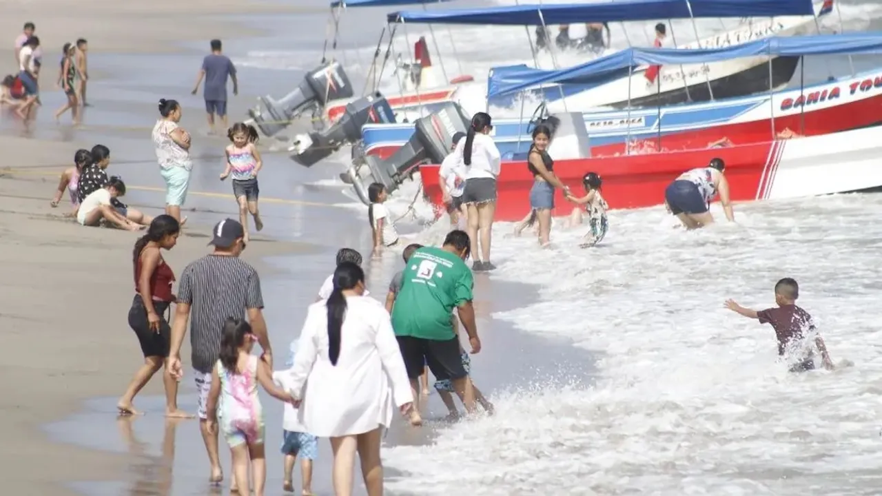Bañistas disfrutan en la orilla del mar junto a varias lanchas a motor estacionadas en la arena de una playa concurrida.