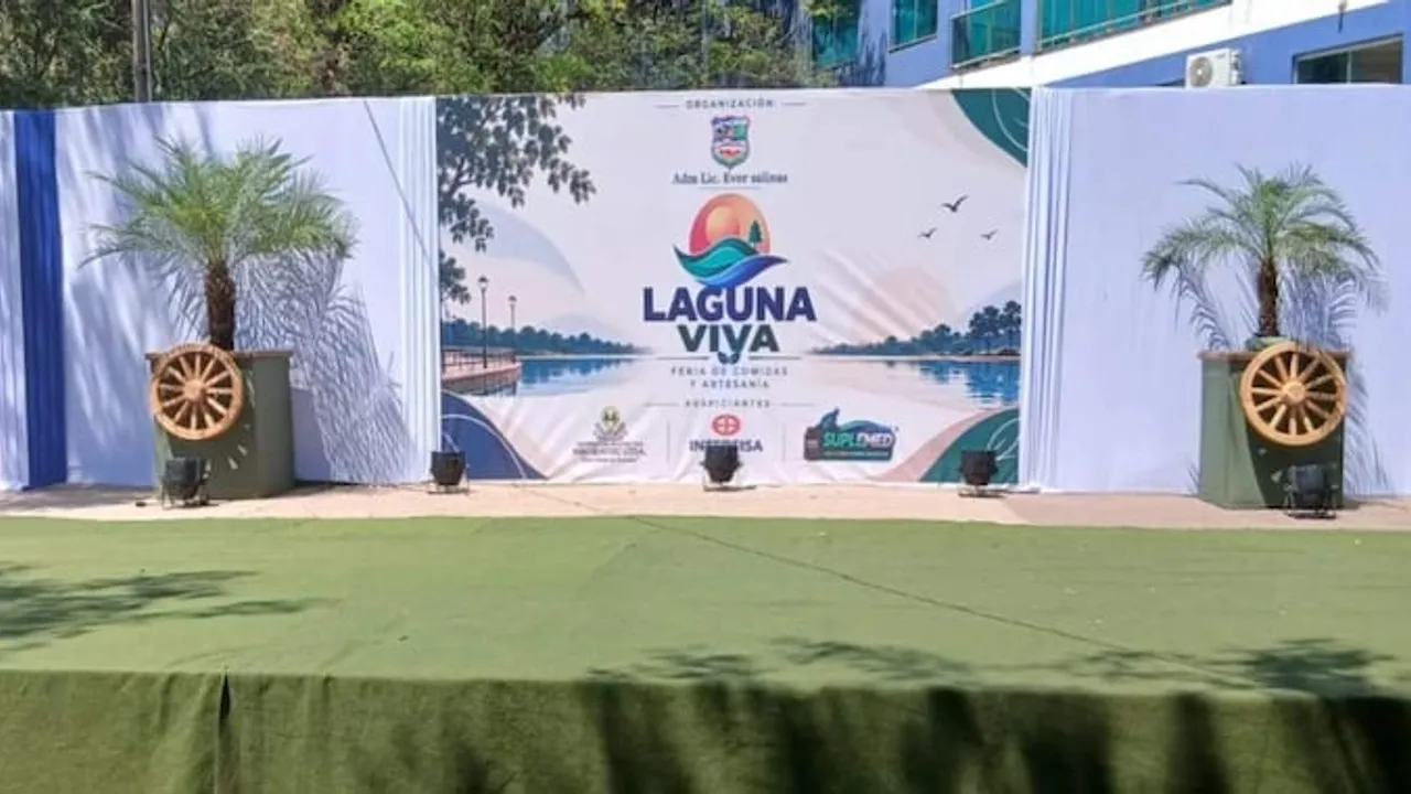 Escenario al aire libre con cartel del festival Laguna Viva flanqueado por plantas ornamentales y ruedas decorativas.