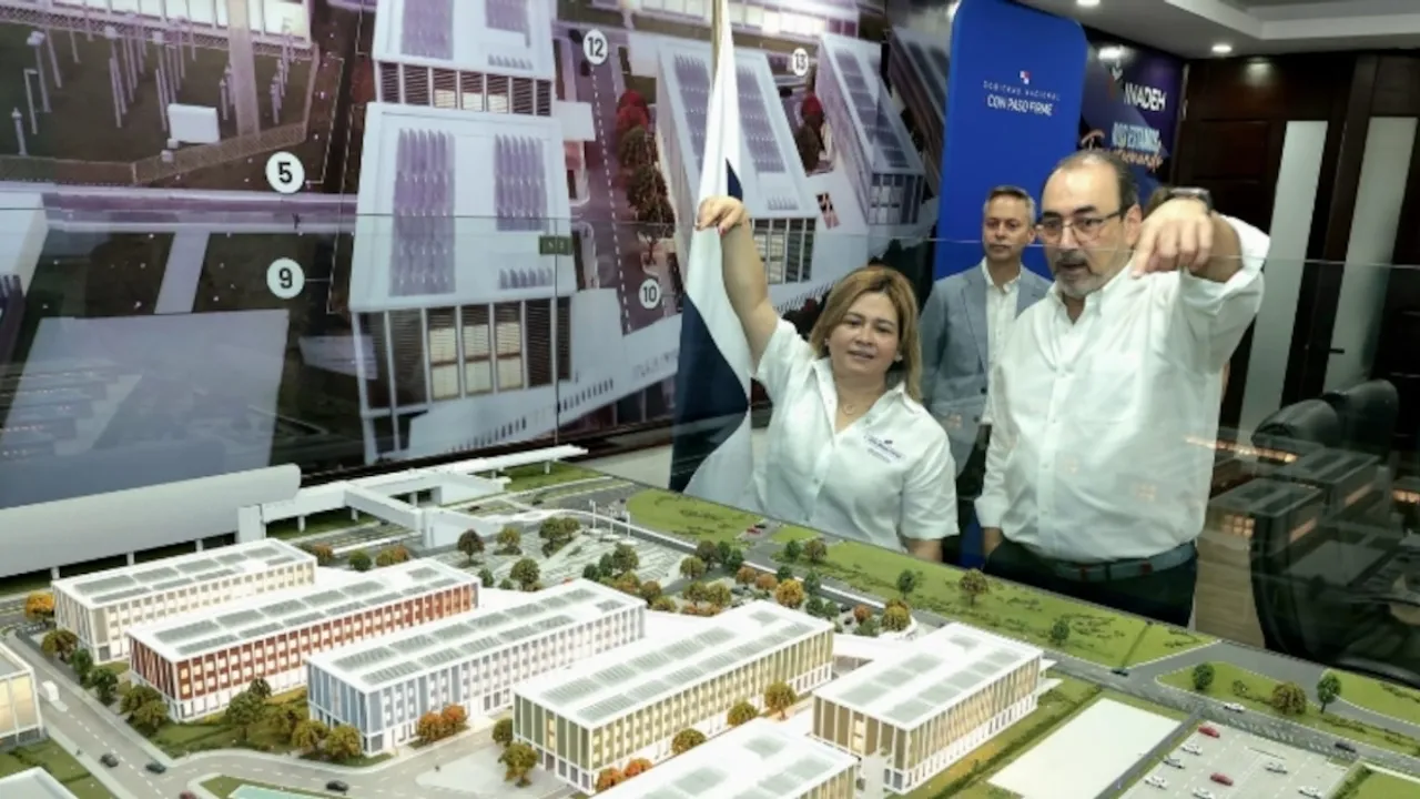 Dos personas observan y señalan con la mano una maqueta arquitectónica detallada de edificios modernos y áreas verdes.