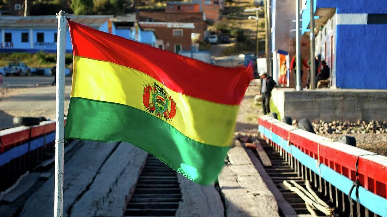 Bandera tricolor de Bolivia con franjas roja, amarilla y verde ondeando sobre un puente de madera al aire libre.