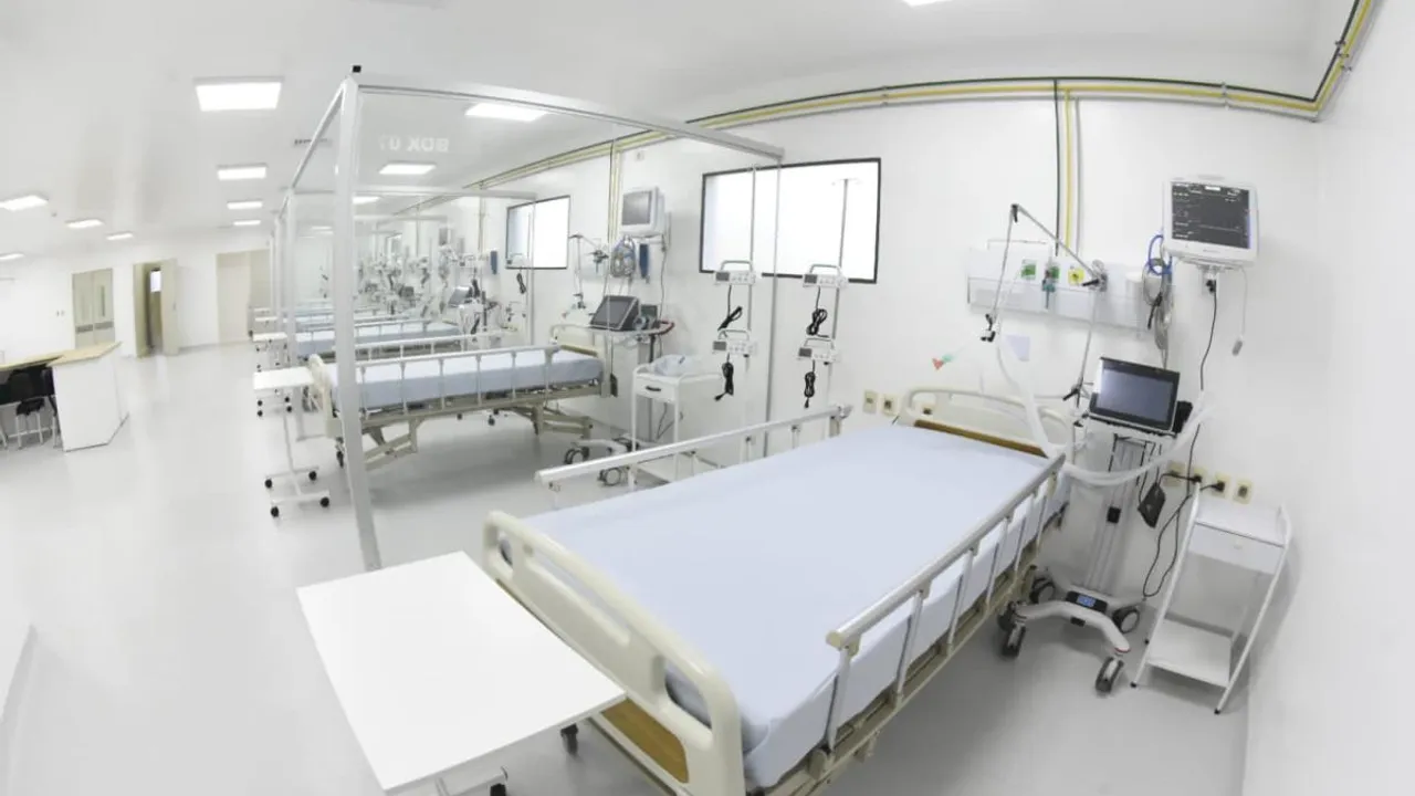 Sala de hospital con varias camas clínicas vacías, monitores digitales y paneles médicos en paredes blancas.