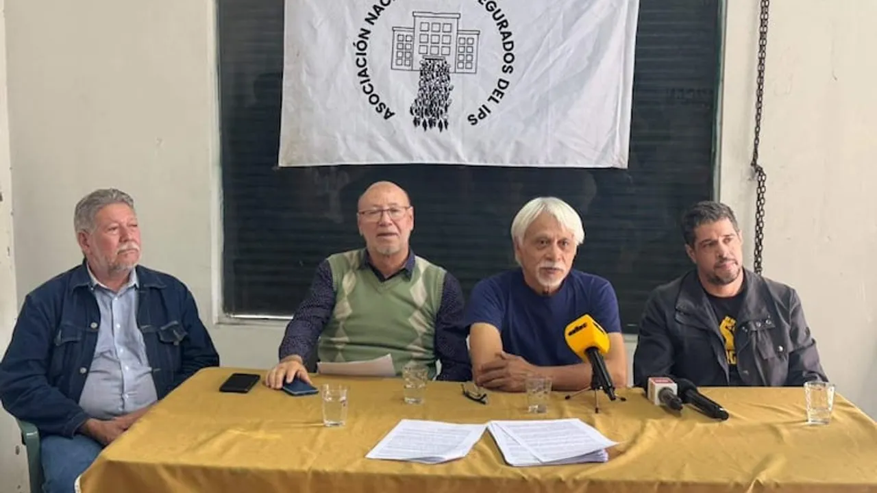 Cuatro dirigentes sentados ante una mesa con micrófonos bajo una pancarta de la Asociación Nacional de Asegurados del IPS.