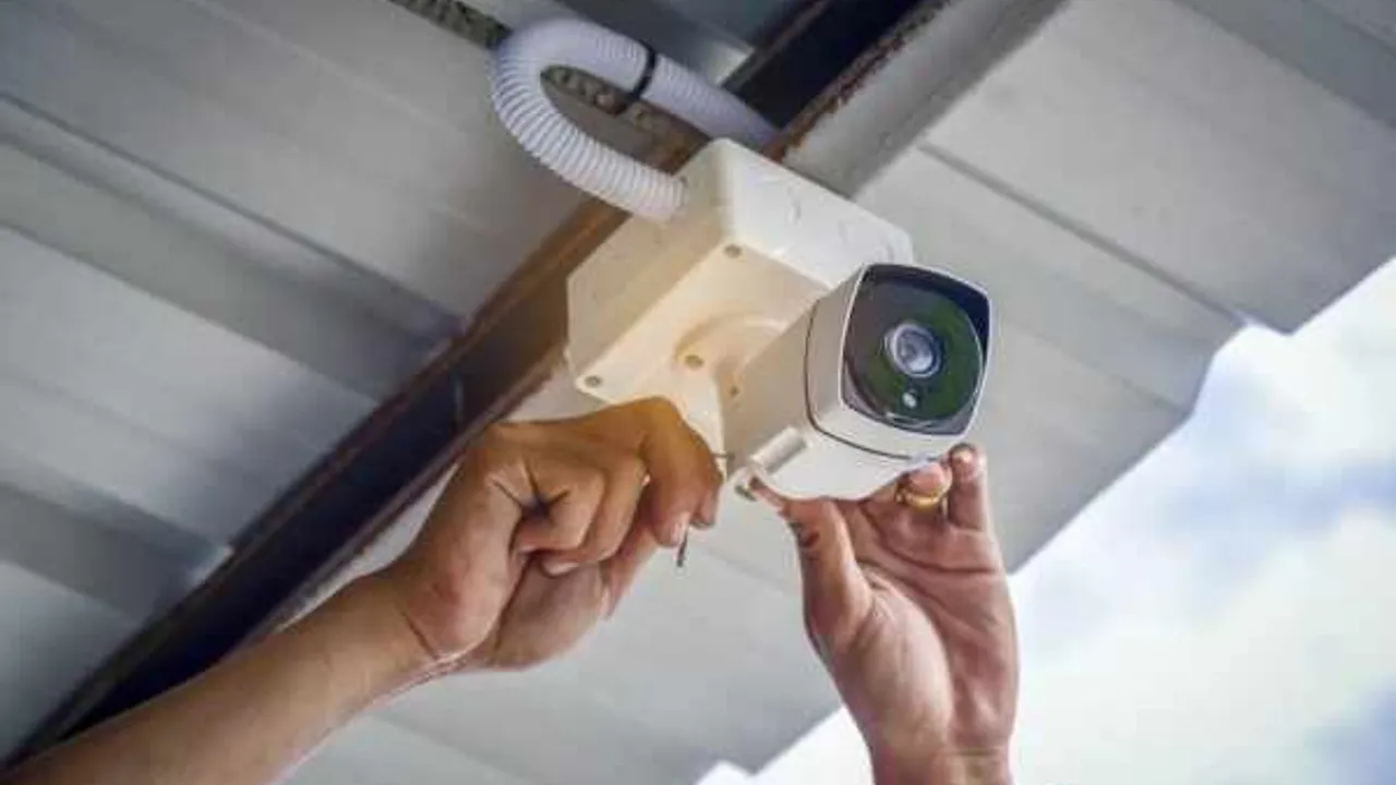Manos de un técnico instalando una cámara de vigilancia blanca bajo una estructura de techo metálico.