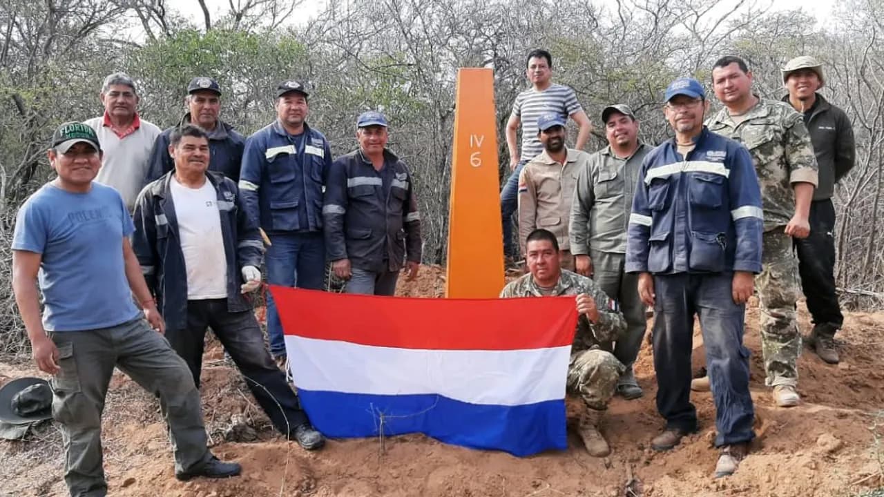 Técnicos y militares posan junto a un hito fronterizo naranja sosteniendo la bandera de Paraguay en el monte chaqueño.