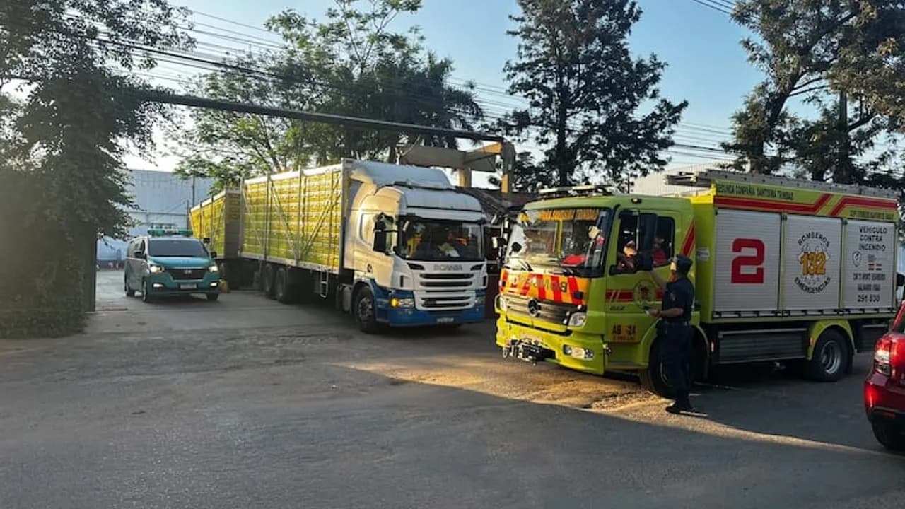 Vehículo de bomberos voluntarios y camiones de carga frente al portón de una fábrica industrial.